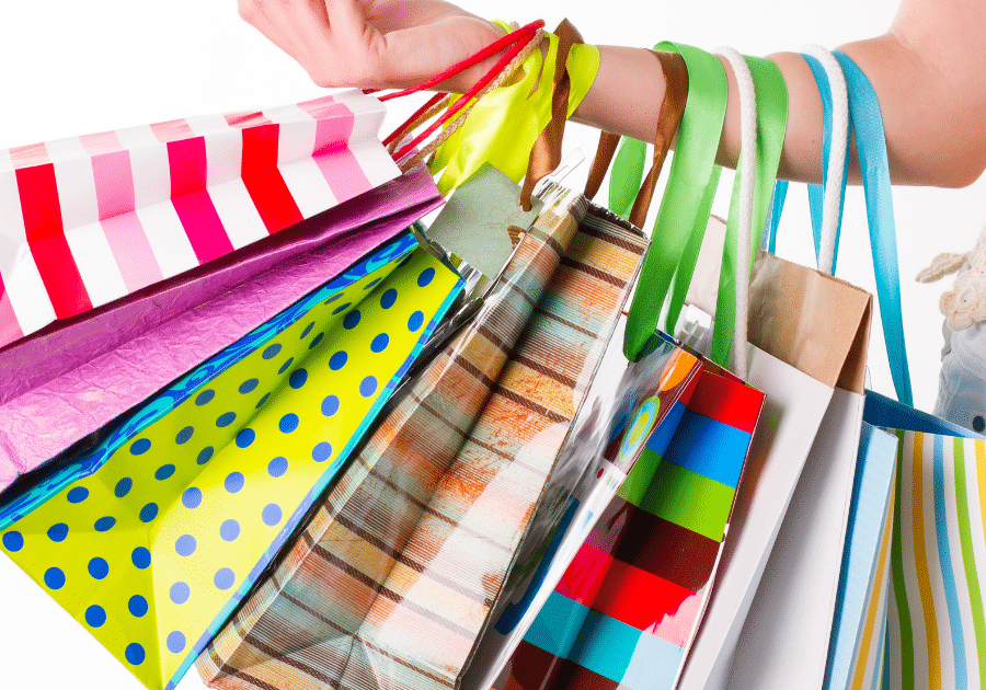 Image is of a hand holding a variety of brightly colored shopping bags to represent the customer service experience