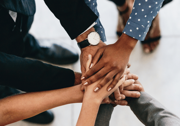 Image shows a diverse group of hands coming together to represent teamwork in a business setting. Image is a visual representation of the teamwork and employee retention.