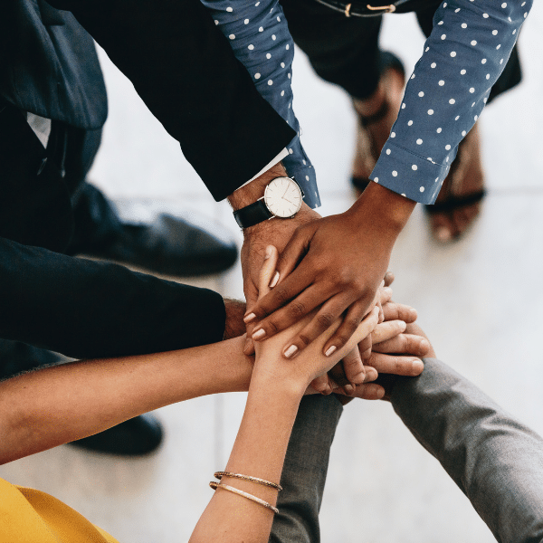 Image shows a diverse group of hands coming together to represent teamwork in a business setting. Image is a visual representation of the teamwork and employee retention.